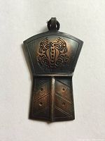 Front view of copper shield pendant showing Northwest Coast design resembling a crab, dark patina and surface wear.