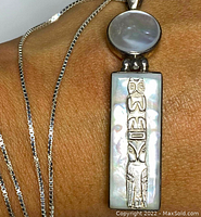 Close-up showing pendant with rectangular abalone inlay and raised silver totem pole design, circular abalone moon on top, worn on wrist for scale.
