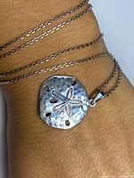 Sterling silver sand dollar pendant necklace on wrist showing pendant shape and chain detail.
