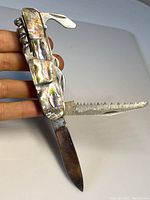 Opened view showing main blade and serrated sawtooth blade extended from abalone handled multi-tool knife.