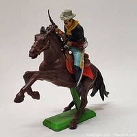 Side profile showing soldier on rearing brown horse with painted uniform and rifle, mounted on green base.