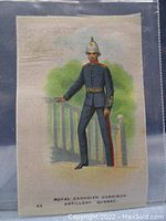 Full view of the antique tobacco silk with color lithograph of a Royal Canadian Garrison Artillery soldier in uniform, standing by a railing with greenery behind.