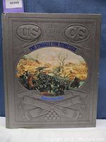 Front cover of the book showing embossed US and CS symbols, along with a colored battle scene illustration and title.