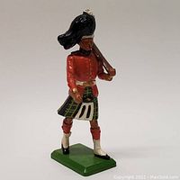 Front view of one metal soldier figurine in kilt holding rifle over shoulder on green base