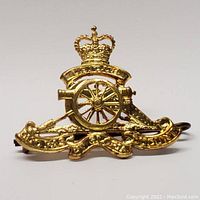Front view of gold-tone Canadian artillery cap badge with detailed Queen's Crown, cannon wheel and barrel, and scroll.
