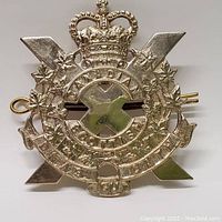 Close-up front view of the Canadian Scottish Regiment cap badge showing intricate details of the crown, maple leaves, and lettering.