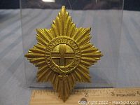 Full front view of the gold tone starburst cap badge with cross emblem and laurel wreath.