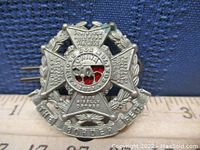 Front view of The Border Regiment cap badge showing detailed metal design, text on crossed flags, central roundel with red enamel.