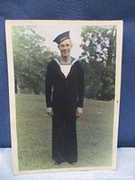Front full-length view of a World War 2 sailor standing outdoors in uniform against a tree and grassy background.