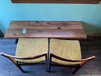Top view of wooden bench showing natural knots, grain, and blemishes on the surface along with two green upholstered chairs below.