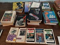 Photo showing multiple stacks of various softcover and hardcover books including poetry, science fiction, and classical titles.