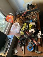 Overview of tools and hardware spread out on a wooden table including clamps, Ryobi power tools, grinding discs, tool belt, and plastic boxes with miscellaneous items