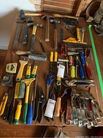 Full view of all tools laid out on wooden surface showing hammers, screwdrivers, scissors, wire strippers, clamps, measuring tape