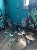 Five cymbals and a chrome tripod stand on wood floor against blue wall.