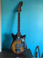 Full view of sunburst electric guitar showing body, neck and headstock against blue wall