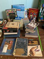 Overview photo of multiple assorted books in worn condition arranged on a table, titles visible include gardening, cooking, classic tales, dog training, and others.