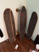 Three boards side by side: one longboard with wheels and two skateboard decks with black grip tape and wear.