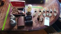 Overview of all items on table including Philishave razor in open case, binoculars with case, light bulbs, two crocodile head figurines and metal leaf pendants.