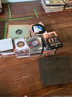 A wide view showing stacks of vinyl records, a box of CDs, a cassette tape in case, and a hardcover book titled 'OZ The Authorized Fanzine'.