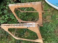 Pair of wooden saw horses placed on grass, showing the rectangular frames with paint splatters.