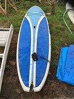 Full view of the blue and white universal stand up paddle board showing the overall shape, length, and condition, as well as the attached ankle strap leash near the tail area.