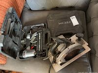 Both tools placed on fabric surface, stapler inside branded ROK case, circular saw beside it.