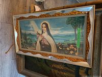 Full view of the framed Christian-themed print laid on floor showing nun holding roses with scenic landscape background.