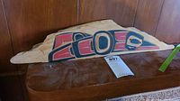 Front view of a rectangular natural wood slab with a painted and carved raven design in red, black, and blue. Shows overall appearance and size relative to background.