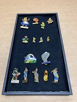 Full display of all 14 pins arranged on black felt-lined tray, showing all characters from Alice in Wonderland, Three Little Pigs, and Wizard of Oz.