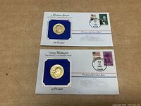 Two gold plated coins mounted on blue background affixed to commemorative envelopes with stamps and postmarks.