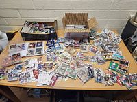 Wide shot of a large assortment of sports cards spread across a table, including stacks and loose cards from multiple sports and brands.