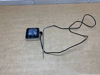 Full view of KitchenAid digital food thermometer with connected temperature probe and display on, placed on a plain beige surface.