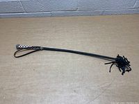 Full view of black leather whip with braided handle and multiple tails, lying on table.