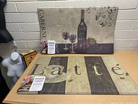 Photo showing two anti-fatigue kitchen mats: one with wine bottle and glasses design, the other with 'Latte' and coffee cup design, both new with tags.