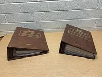 Two brown hardcover vintage stamp books titled 'Golden Replicas United States Stamps' by Robert J. Aulicino with gold embossed text, lying closed on a wooden table.