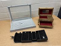 Photo showing all three jewelry boxes on a table, including grey velvet ring tray, gold-tone music box, and black multi-compartment box