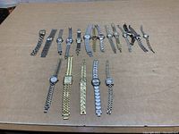 Overview photo of 15 bracelet watches laid on beige surface showing variety in styles, colors, and face shapes.