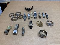 Lot of 17 women's bracelet watches laid out on a surface, including various metal stretch and metal link band watches as well as a black silicone band watch.