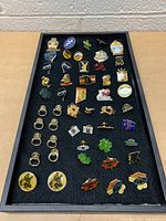 Photo of tray with a variety of lapel pins featuring cartoon characters, shamrocks, slogans, and symbols.