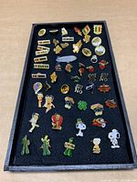Overview of all lapel pins mounted on black board showing a variety of cartoon characters, slogans and animal pins.