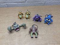 Six Pokémon keychains including two Dragonite figures, Nidorino, Nidoqueen, Geodude, Hitmonlee on wooden surface.