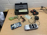 Vintage electric car toy, wired controllers, decals, toolbox, and electric parts displayed on table.