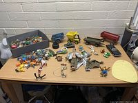 Wide shot of whole lot on table showing various metal truck beds, wagons, action figures, and many small toy figures spread out.