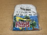 White In-N-Out Burger XL t-shirt still in original sealed plastic packaging showing size and brand logo.
