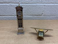 Both clocks together showing detail and size comparison on a wooden surface with white brick wall background