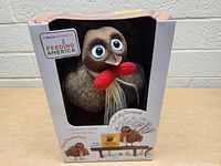 Front view of the boxed Talking Table Thanksgiving turkey hand puppet with finger feathers and game cards/dice.