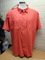 Front view of coral short sleeve men's Under Armour shirt on mannequin showing button-up front and vertical chest pockets.