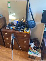 Full view of lot showing cameras, lenses, flash units, bags on dresser and tripod in front.