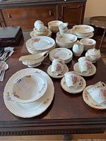 Photo showing the Grindley Cream Ware Rose Bouquet pattern dinnerware including plates, cups, saucers, sugar bowl, creamer, and other pieces arranged on a wooden table.