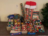 Overview of lot items including boxes of glass ornaments, tinsel garlands, wrapping paper rolls, Santa hats and a string of lights